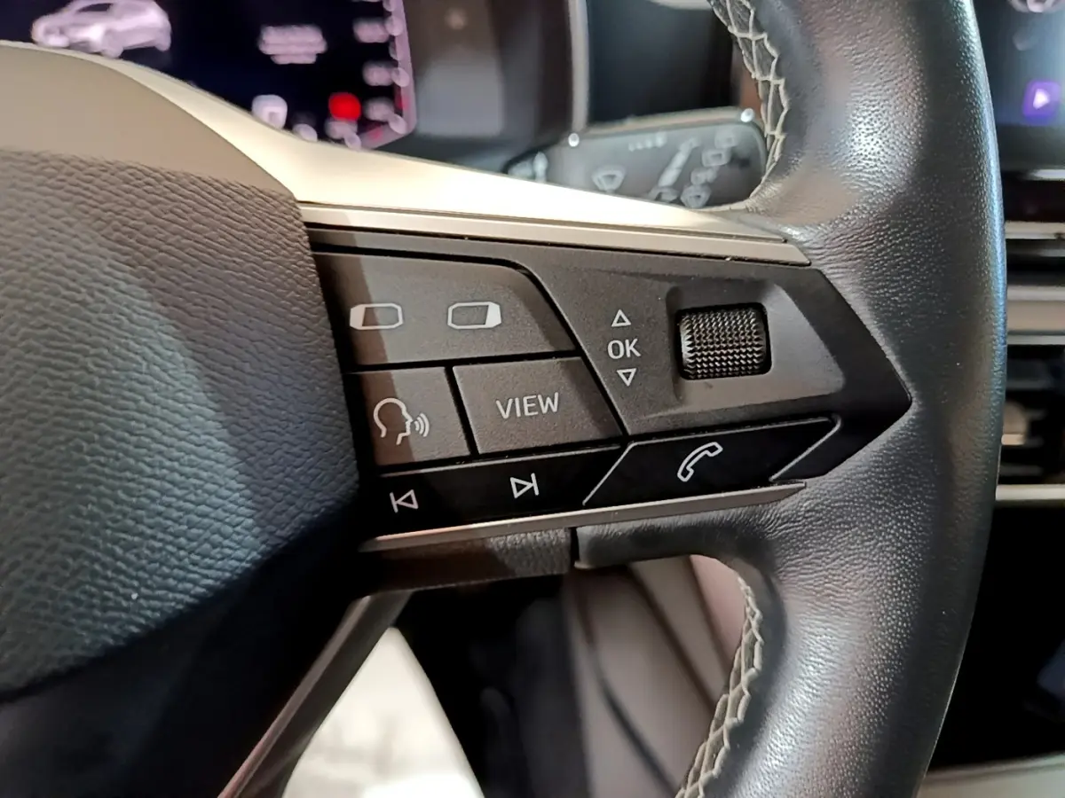 Gros plan sur les commandes au volant en cuir noir du SEAT Leon 2023, avec boutons multifonctions et molette tactile.