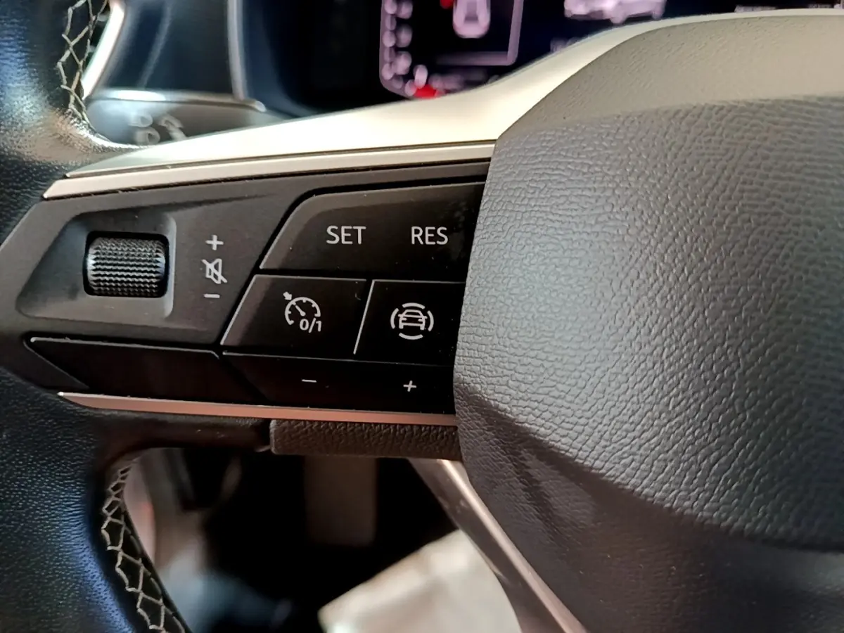 Gros plan sur les commandes de régulateur de vitesse au volant cuir noir du SEAT Leon gris foncé 2023.