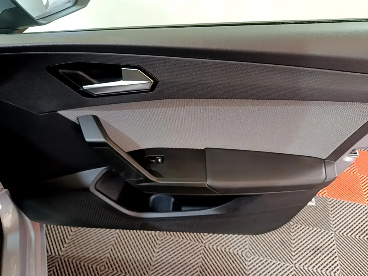 Intérieur côté gauche de la porte d'une SEAT LEON gris foncé, avec poignée argentée et panneau textile gris.