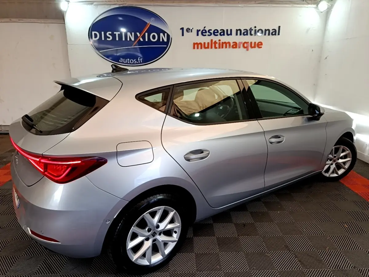 SEAT Leon gris clair vue 3/4 arrière droit dans un showroom avec feux arrière LED allumés.