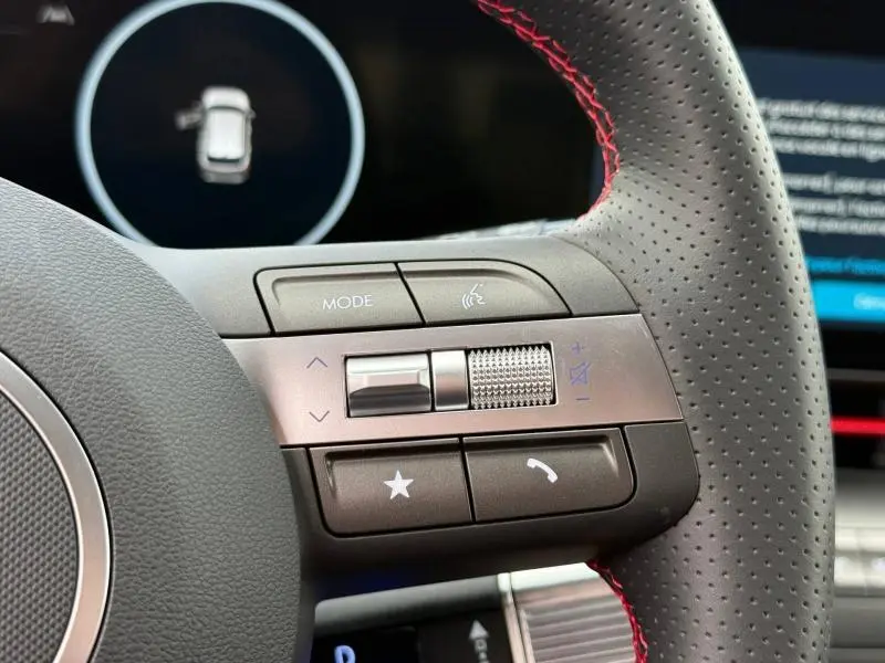 Gros plan sur les commandes audio et vocales du volant cuir perforé avec surpiqûres rouges du Hyundai Kona Cyber Gray 2025.