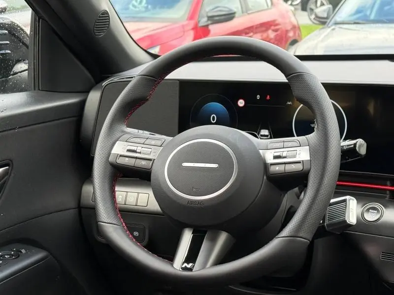 Vue rapprochée du volant cuir noir avec surpiqûres rouges et tableau de bord numérique du Hyundai Kona 2025.