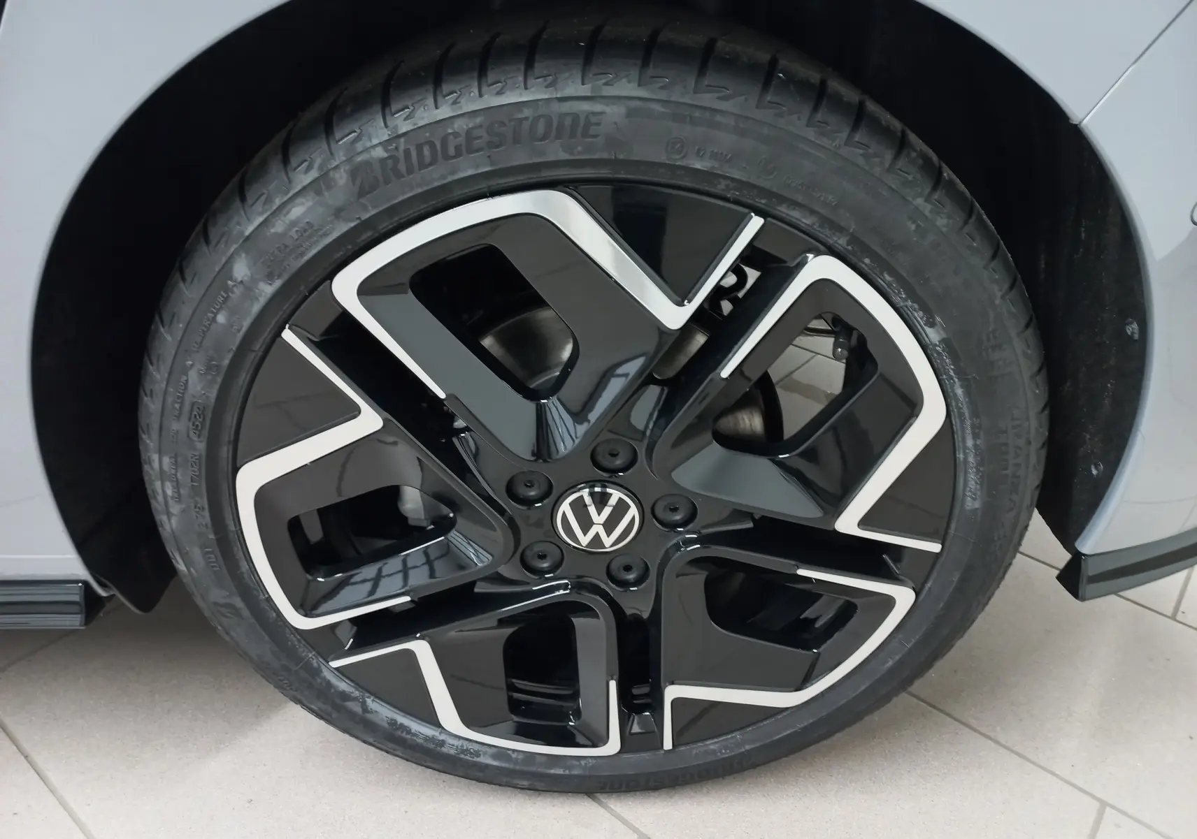 Gros plan sur la roue avant droite d’une Volkswagen Golf gris lunaire avec jante noire et argentée au design moderne.