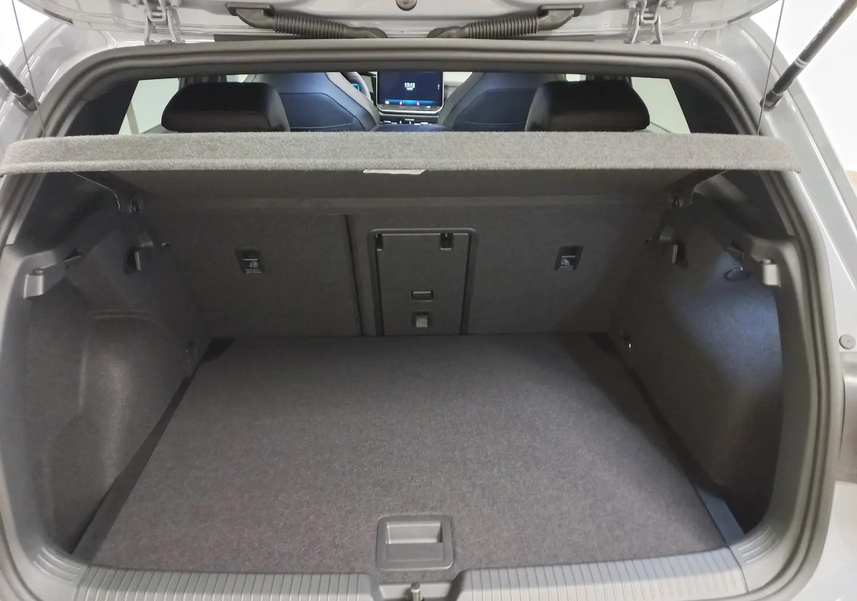 Coffre ouvert vu de l'arrière d'une Volkswagen Golf gris lunaire avec banquette arrière et tablette cache-bagages.