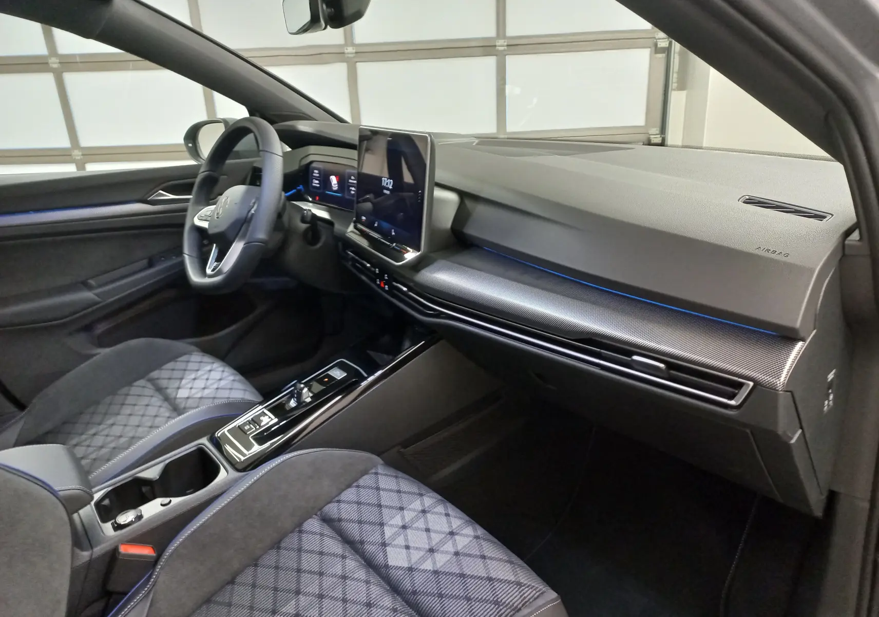 Vue intérieure côté conducteur de la Volkswagen Golf 2.0 TDI R-Line 2026 avec sièges gris à motifs et tableau de bord moderne.