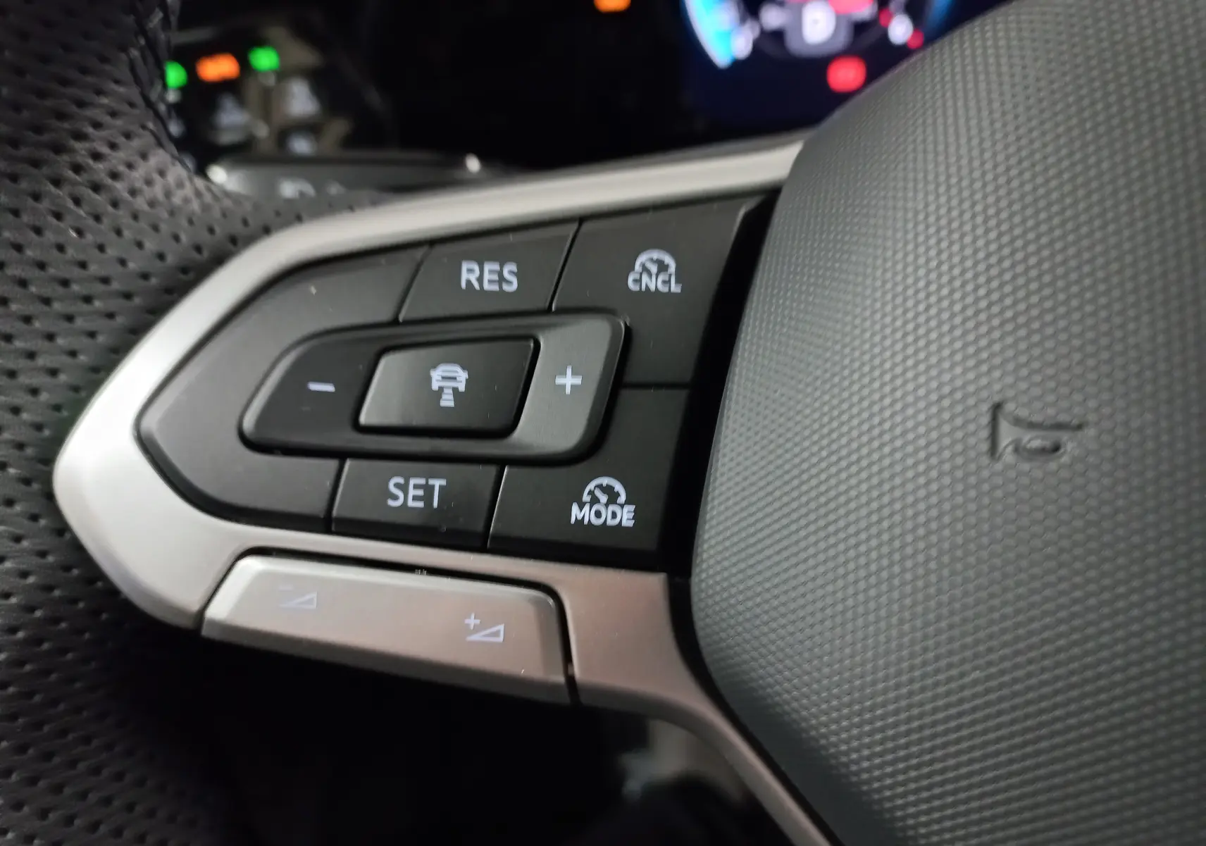 Gros plan sur les commandes de régulateur de vitesse au volant cuir perforé d'une Volkswagen Golf gris lunaire 2026.