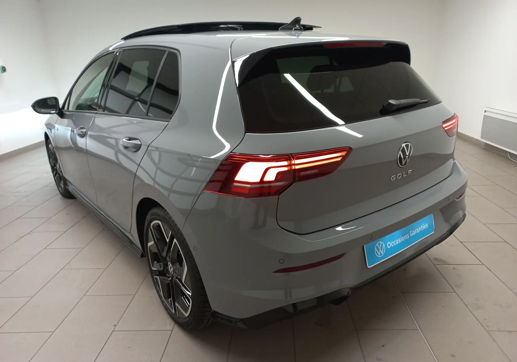 Vue 3/4 arrière droite d'une Volkswagen Golf 2.0 TDI R-Line gris lunaire avec toit ouvrant panoramique en intérieur showroom.