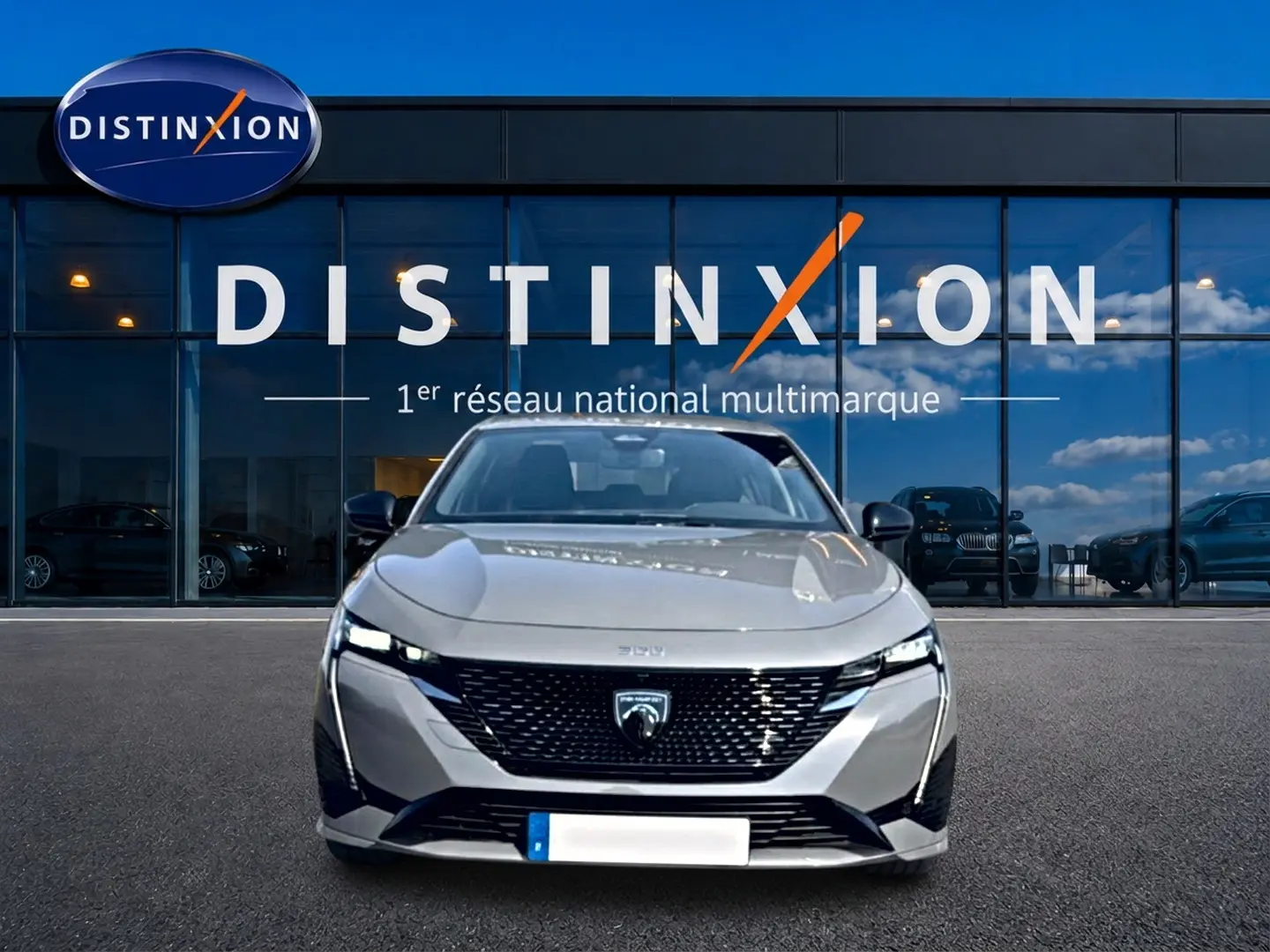 Vue avant d'une Peugeot 308 gris métallisé 2025 garée devant une vitrine avec logo Distinxion.
