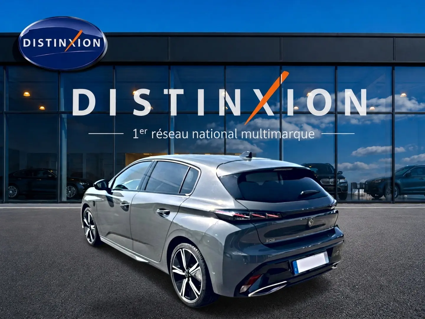 Peugeot 308 gris en 3/4 arrière droit, avec vitres surteintées et jantes alliage distinctives, devant une vitrine Distinxion.