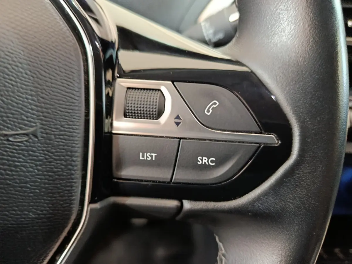 Gros plan sur les commandes gauche du volant cuir noir du Peugeot 3008 bleu, boutons appel et réglages audio visibles.