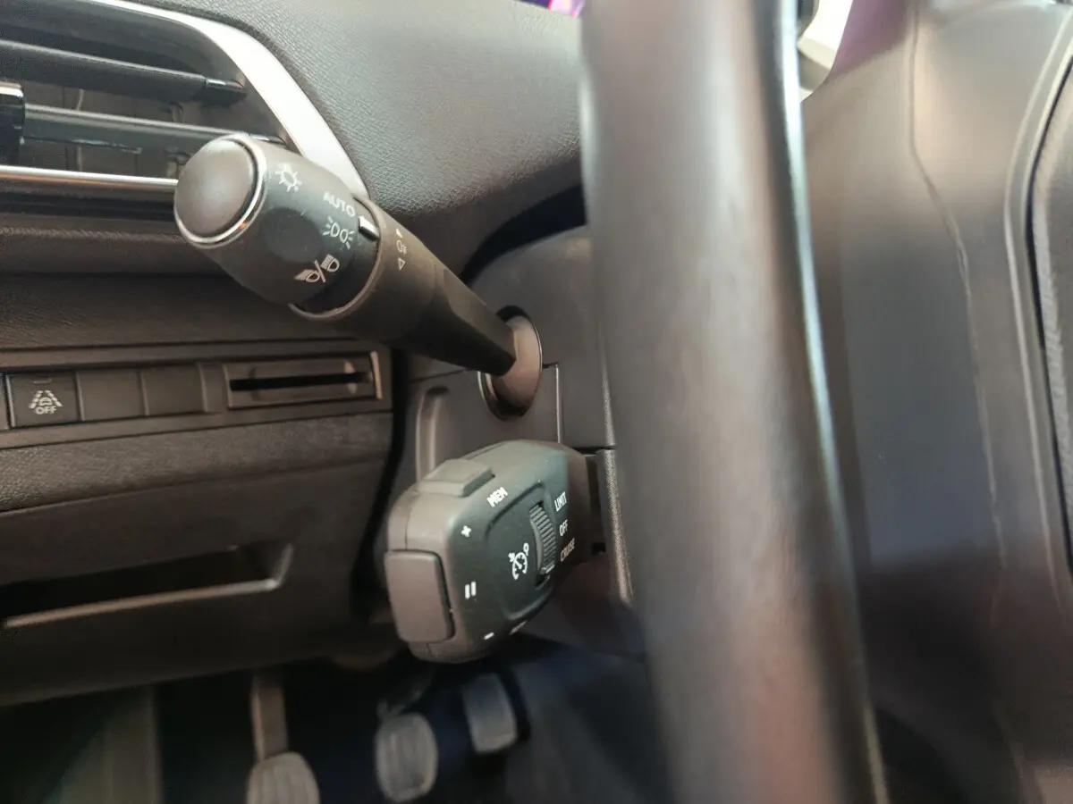 Gros plan sur les commandes au volant noir du Peugeot 3008 bleu, mettant en valeur le régulateur de vitesse et les phares automatiques.