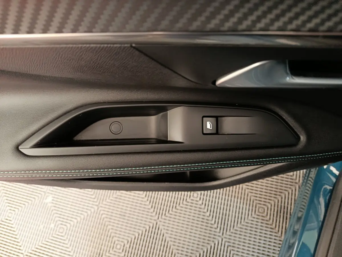 Gros plan sur la poignée intérieure et commande de vitre côté gauche d’un Peugeot 3008 bleu 2022.