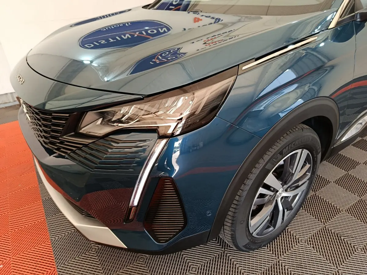 Vue 3/4 avant droit d'un Peugeot 3008 bleu avec phares LED et jante alliage visible sur sol en damier.