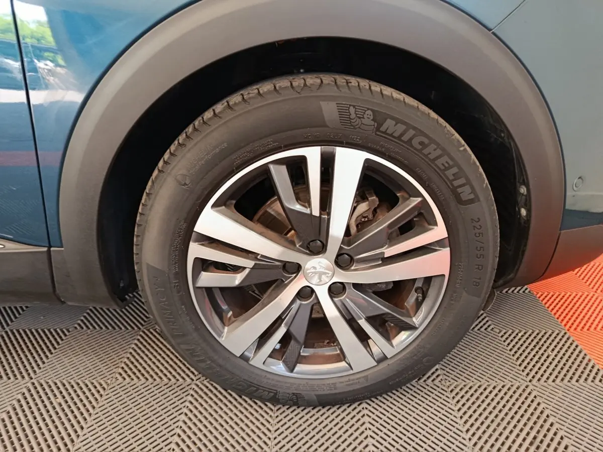 Gros plan sur la roue avant gauche du Peugeot 3008 bleu, mettant en valeur la jante alliage et le pneu Michelin.