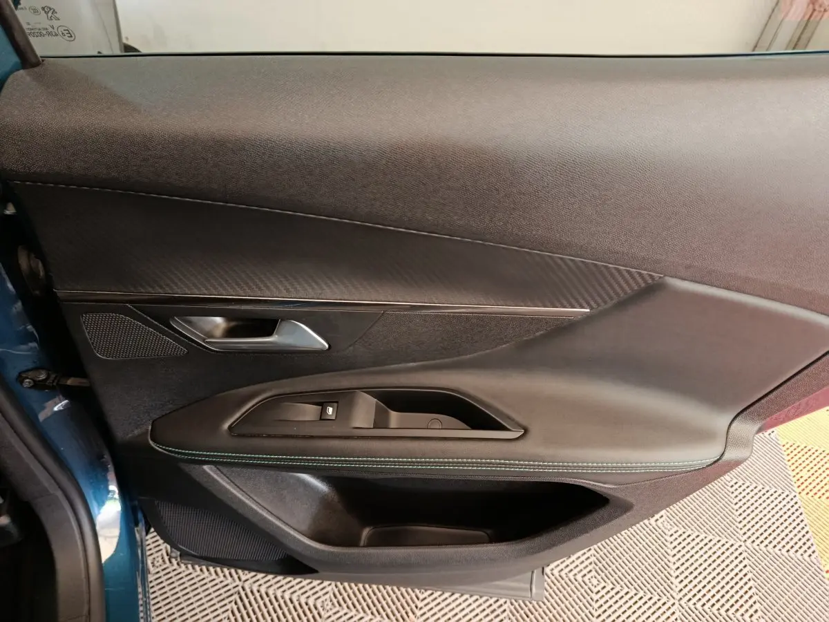 Vue rapprochée de la porte avant gauche du Peugeot 3008 bleu, avec garniture noire et surpiqûres vertes visibles.