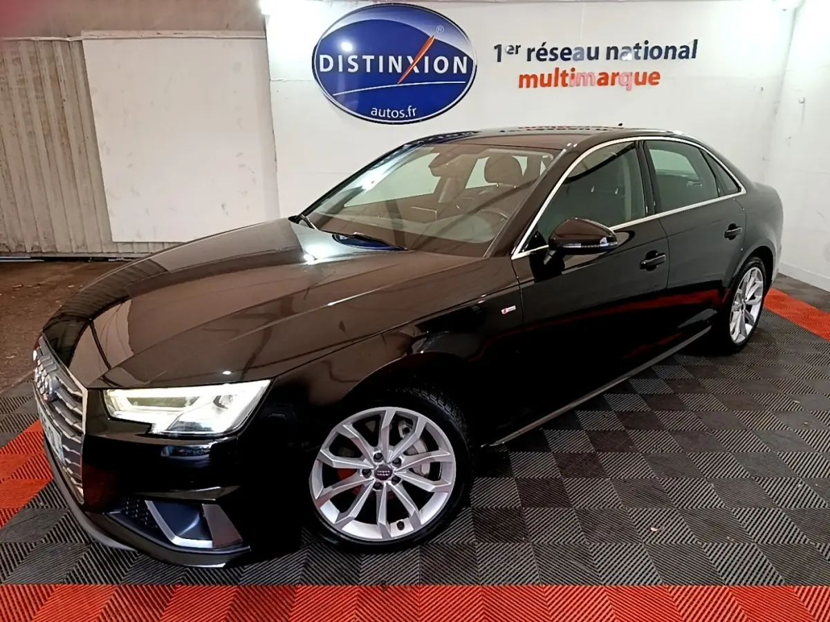 Audi A4 noire en 3/4 avant droit, avec jantes argentées et phares LED allumés en intérieur showroom.
