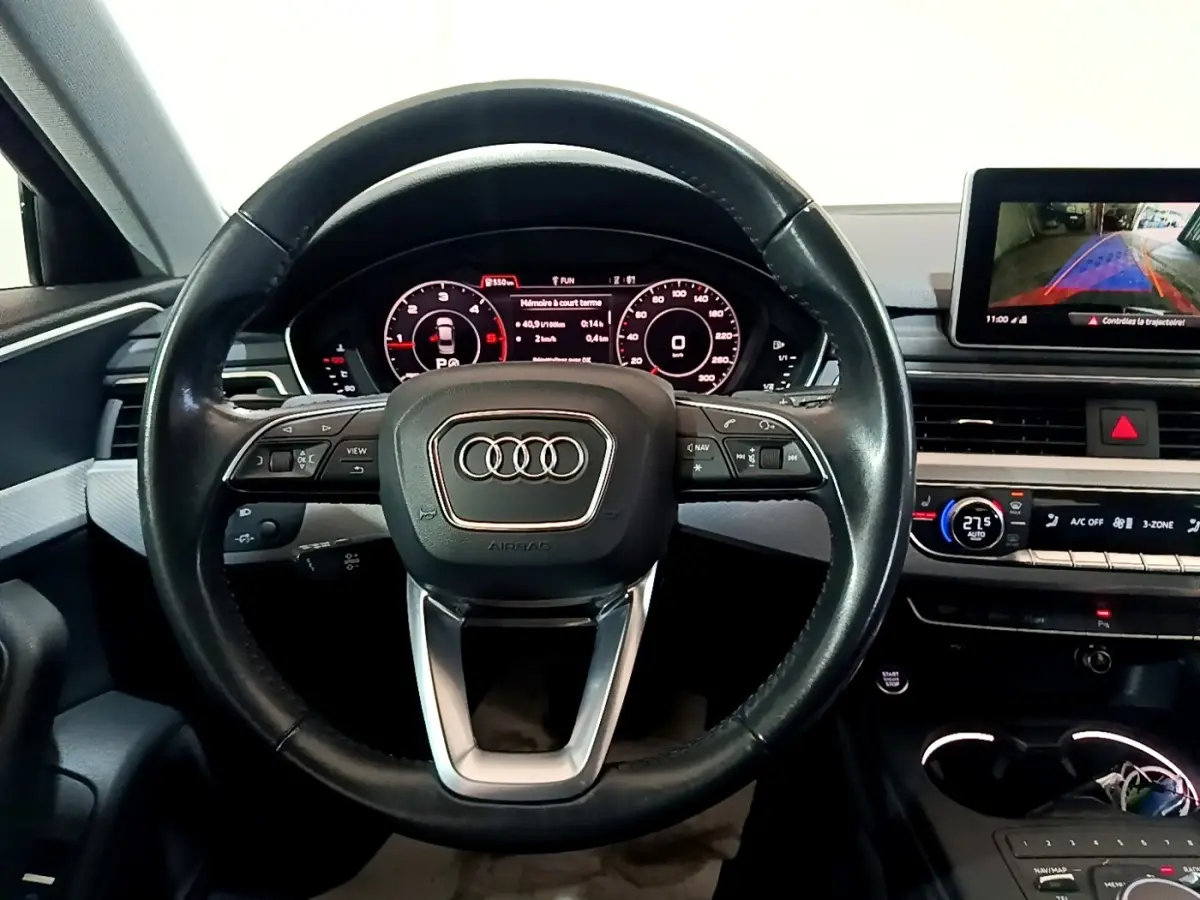 Vue intérieure centrée sur le volant cuir noir d'Audi A4 40 TDI avec tableau de bord digital et écran multimédia arrière.