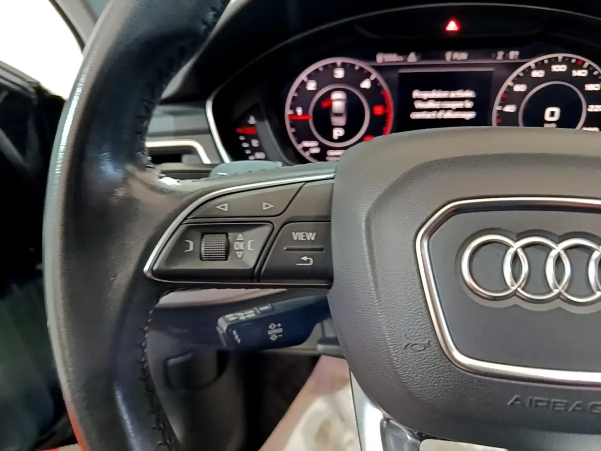 Gros plan sur le volant cuir noir de l'Audi A4 40 TDI 190 Quat S tronic Design Luxe avec commandes multifonctions visibles.