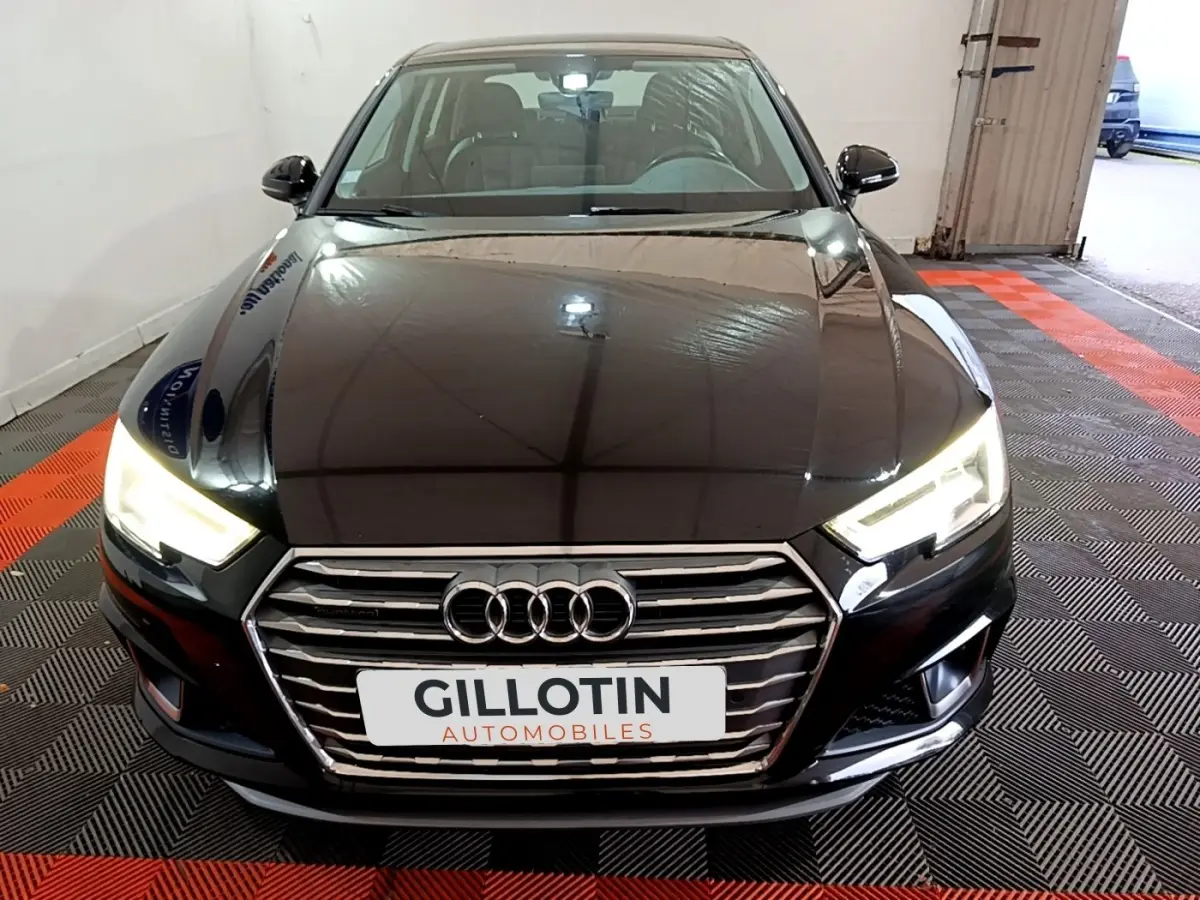 Vue avant d'une Audi A4 noire avec phares LED allumés et calandre chromée dans un garage.