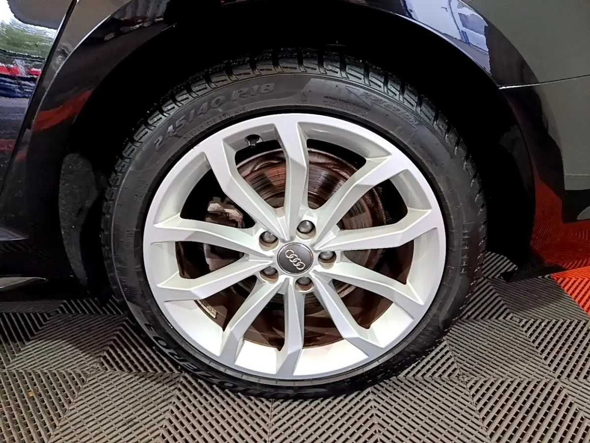 Gros plan sur la roue avant droite d’une Audi A4 noire 2018 avec jante en alliage argentée et logo Audi central.