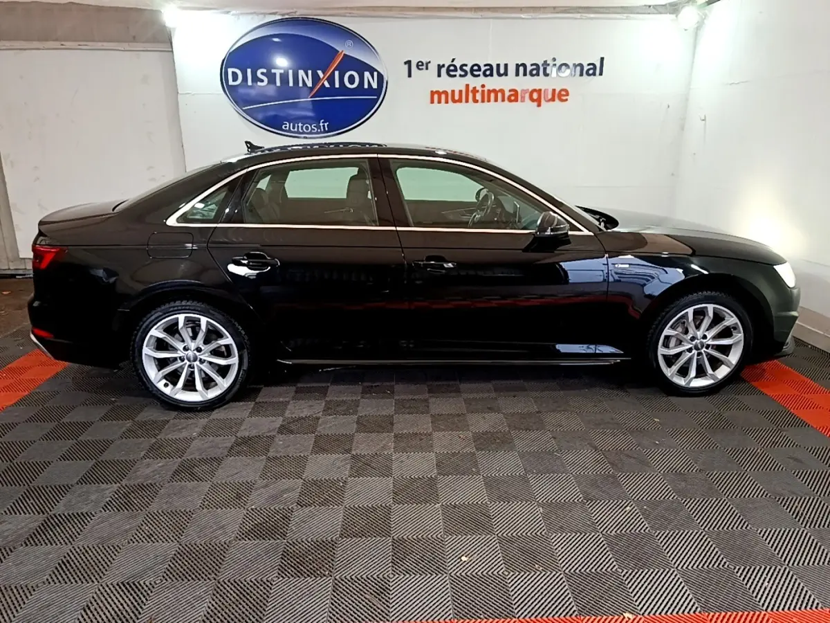 Audi A4 noire 2018 vue de profil côté gauche, stationnée en intérieur sur sol damier gris et rouge.