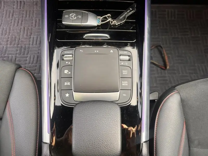 Vue plongeante sur la console centrale noire brillante avec pavé tactile et clé Mercedes sur un intérieur cuir noir avec surpiqûres rouges.