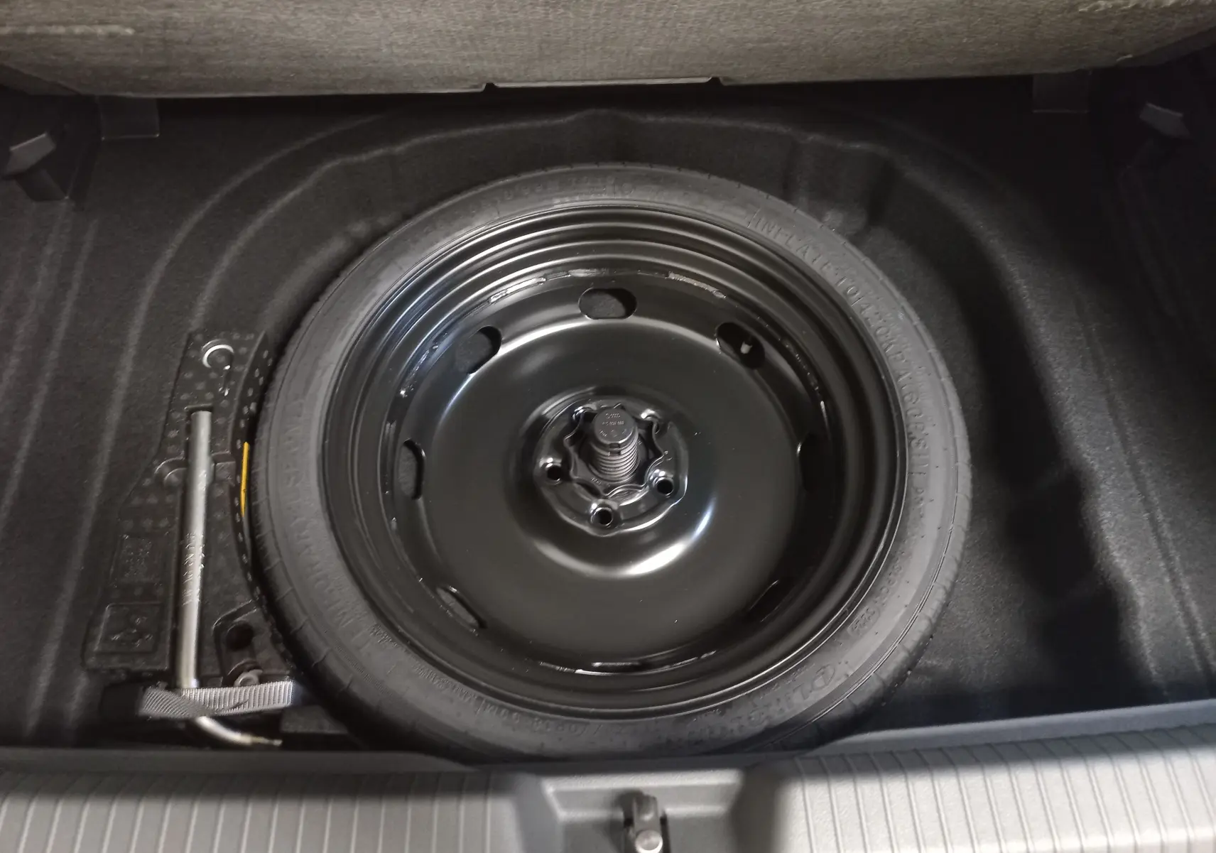 Vue plongeante sur la roue de secours compacte noire et le cric dans le coffre d'une Volkswagen Golf gris lunaire 2026.