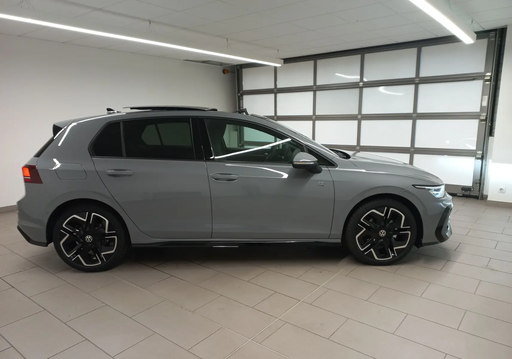 Vue de profil côté gauche d'une Volkswagen Golf 2.0 TDI R-Line gris lunaire avec toit ouvrant panoramique en intérieur showroom.