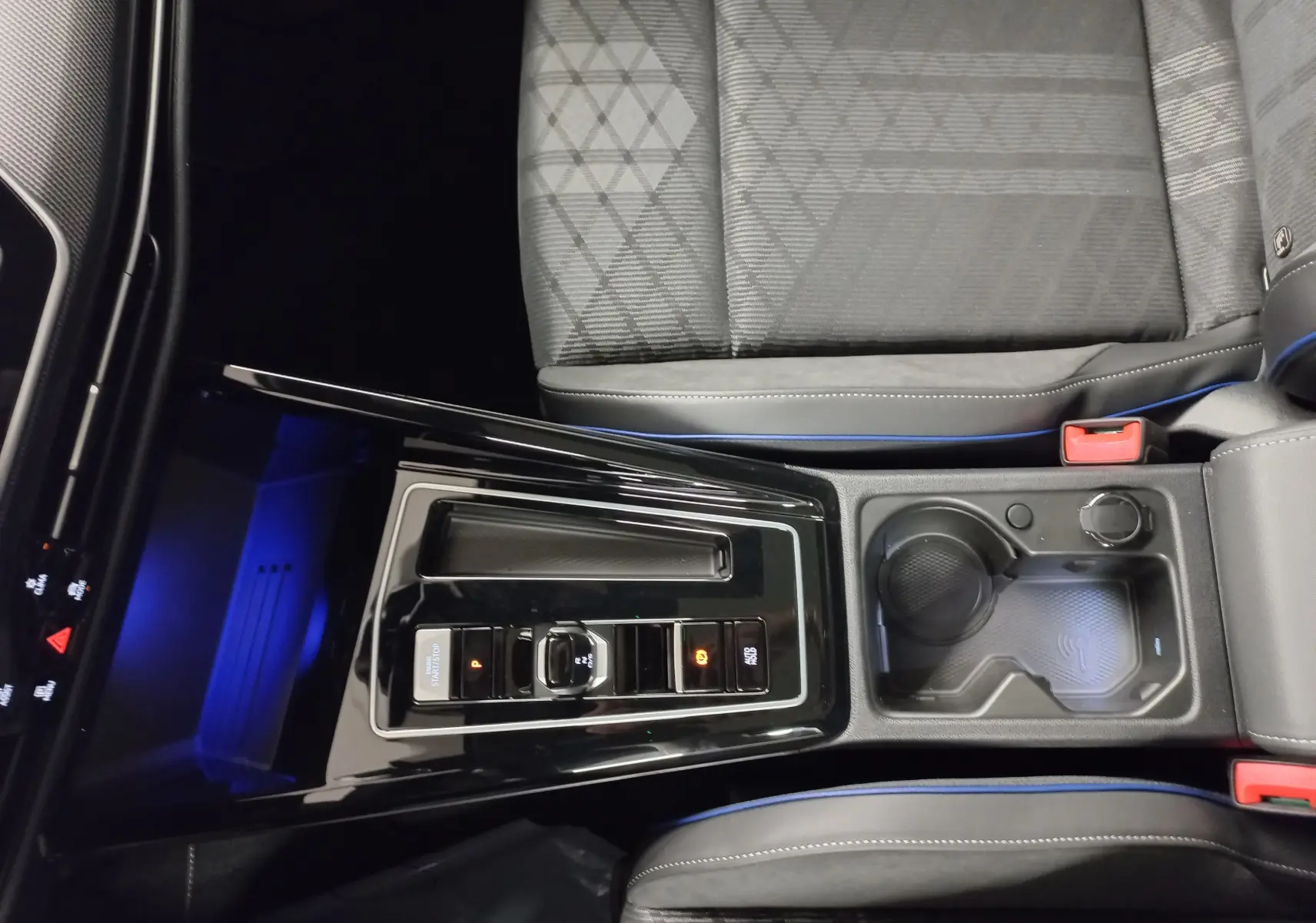 Vue plongeante sur la console centrale noire brillante et les sièges gris à surpiqûres bleues de la Volkswagen Golf 2.0 TDI R-Line.