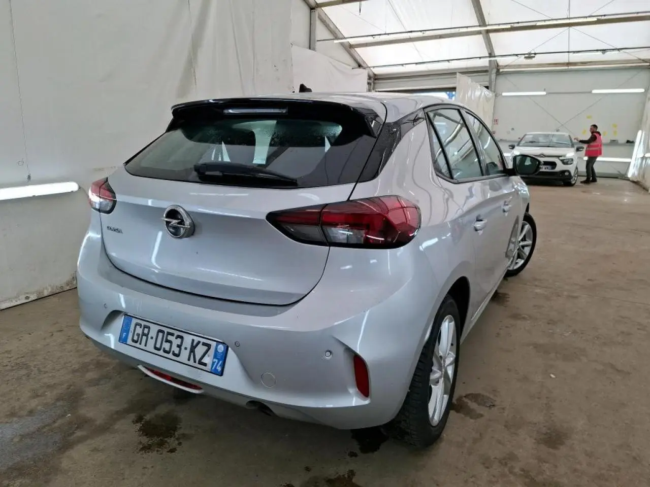 Vue 3/4 arrière droite d'une Opel Corsa gris clair avec jantes alliage 16'' dans un garage fermé.