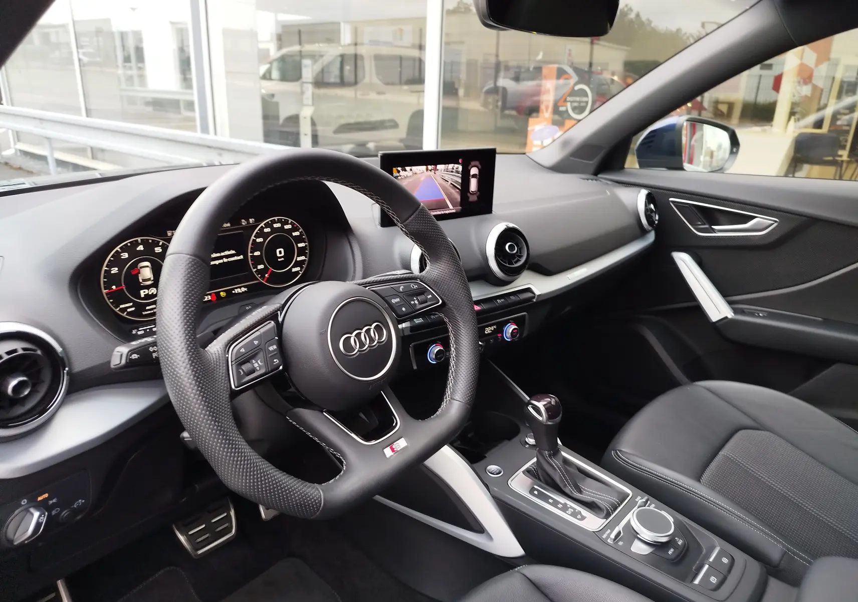 Vue intérieure côté conducteur de l'Audi Q2 35 TFSI 2023, avec volant sport, écran central et sellerie noire.