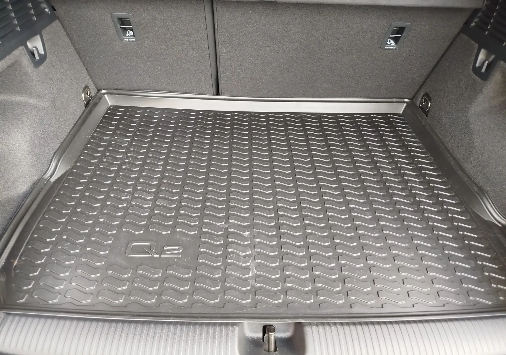 Vue intérieure du coffre de l'Audi Q2 avec tapis de protection noir marqué Q2, sans couleur extérieure visible.