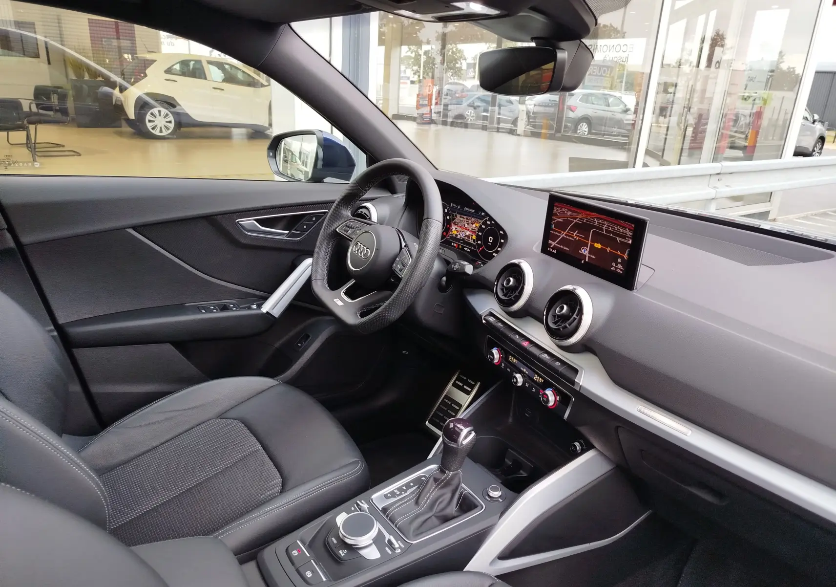 Vue intérieure côté conducteur de l'Audi Q2 35 TFSI 2023, avec tableau de bord moderne et sellerie noire.