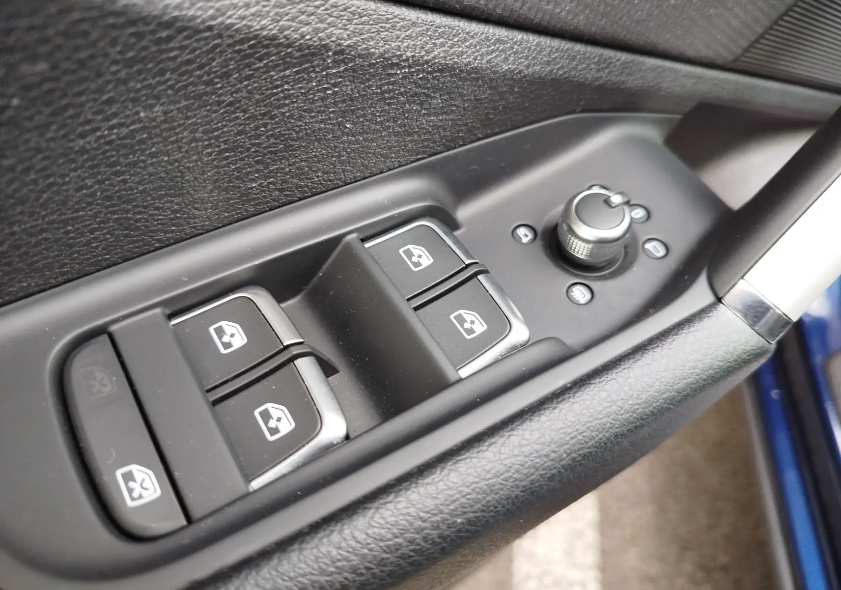 Gros plan sur les commandes de lève-vitres et réglage des rétroviseurs côté conducteur d’un Audi Q2 bleu Navarre 2023.