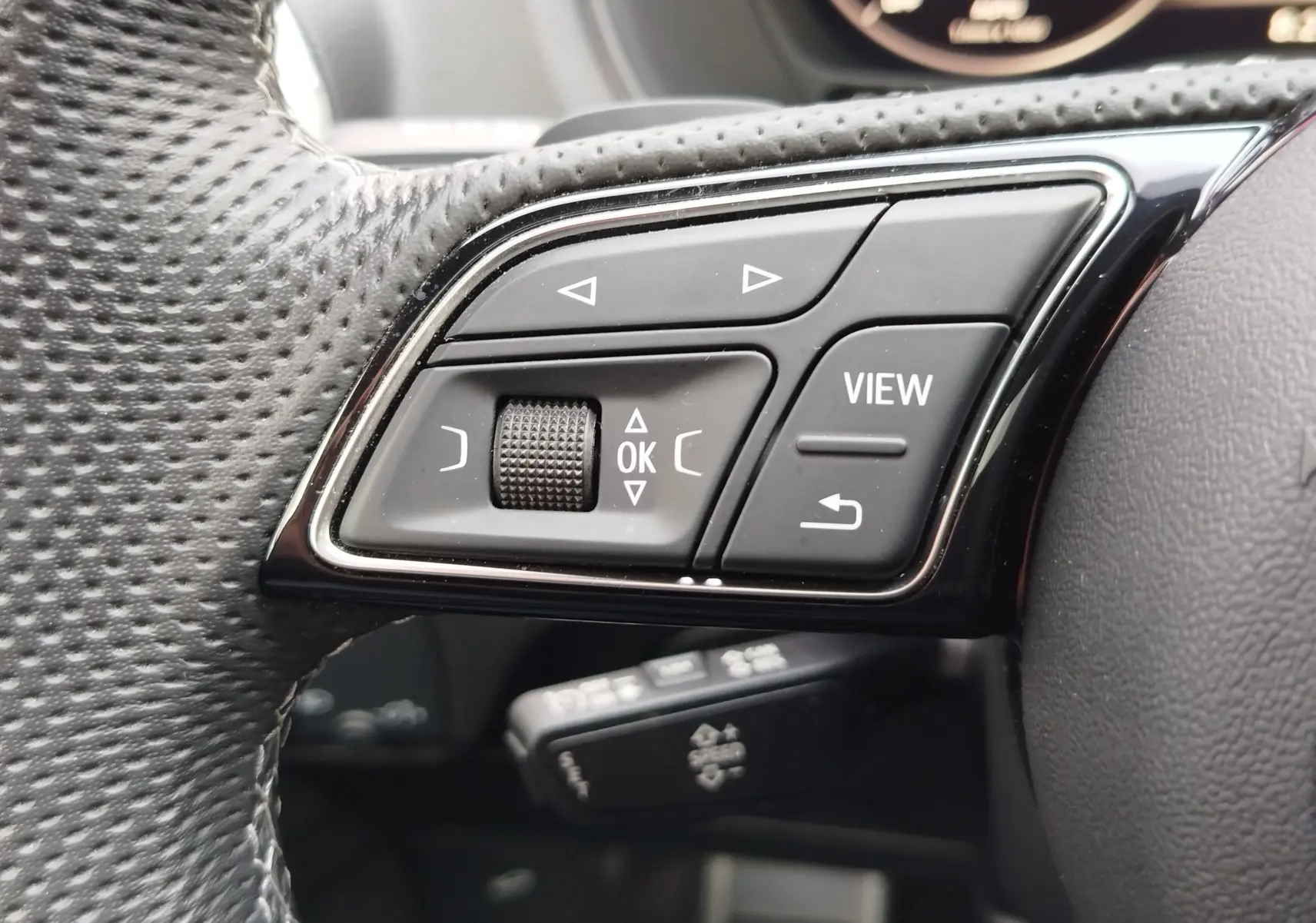 Gros plan sur les commandes gauche du volant noir perforé de l'Audi Q2 35 TFSI 2023, avec boutons de navigation et fonction View.