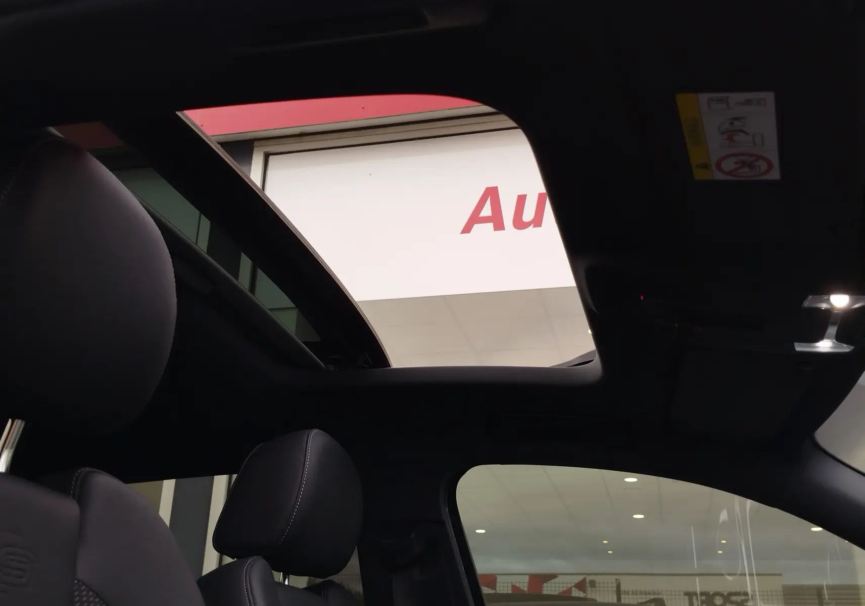 Vue intérieure du toit ouvrant panoramique d'un Audi Q2 35 TFSI bleu Navarre, avec sièges avant en cuir noir.