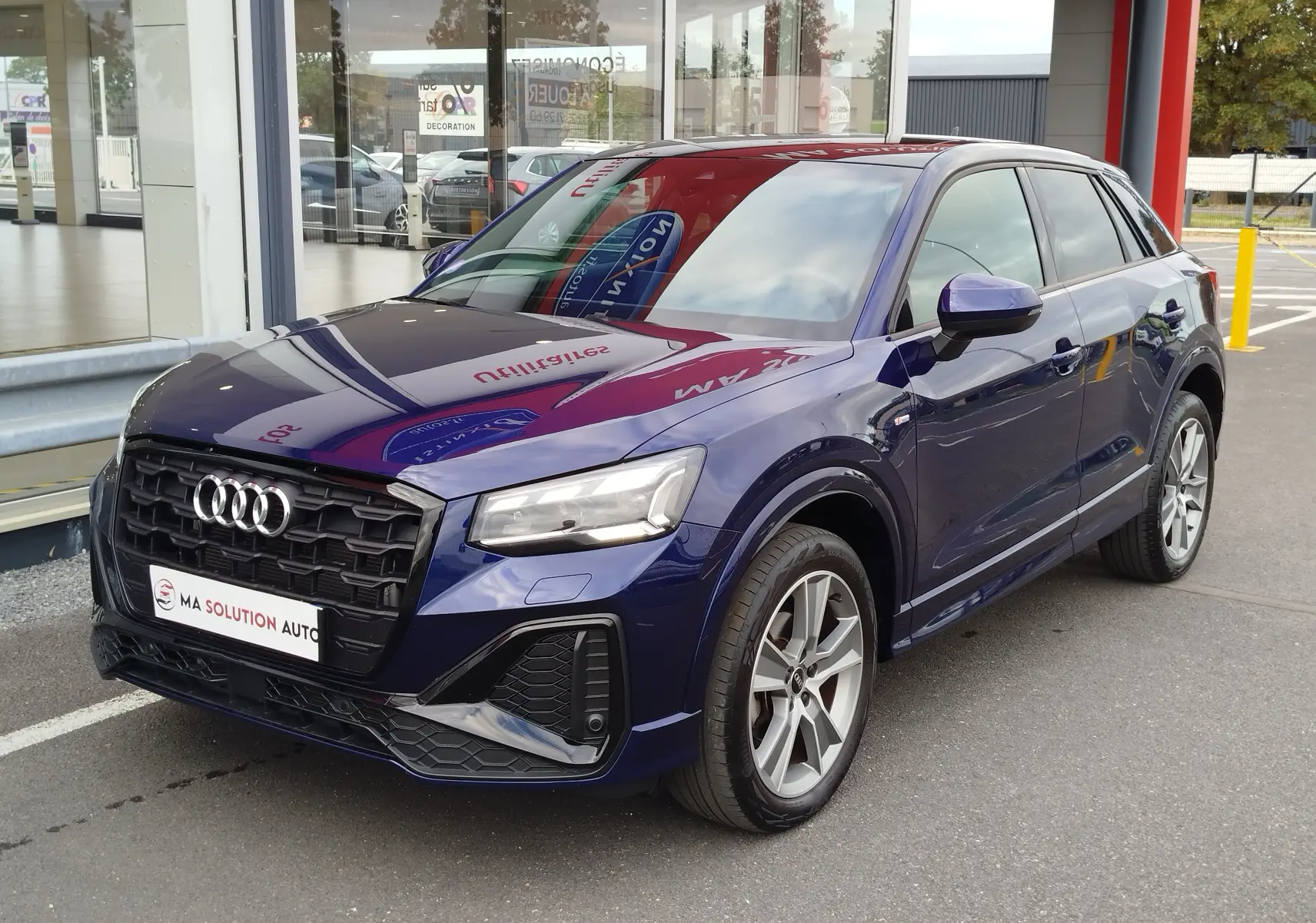 Audi Q2 bleu Navarre en vue 3/4 avant droit, avec calandre noire S line et jantes alliage 18 pouces bicolores.