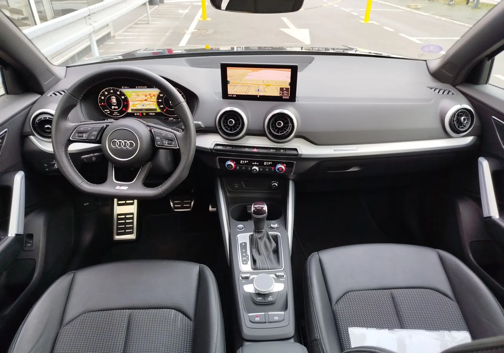 Vue intérieure frontale de l'Audi Q2 35 TFSI 2023 avec tableau de bord noir, volant sport et écran central GPS.