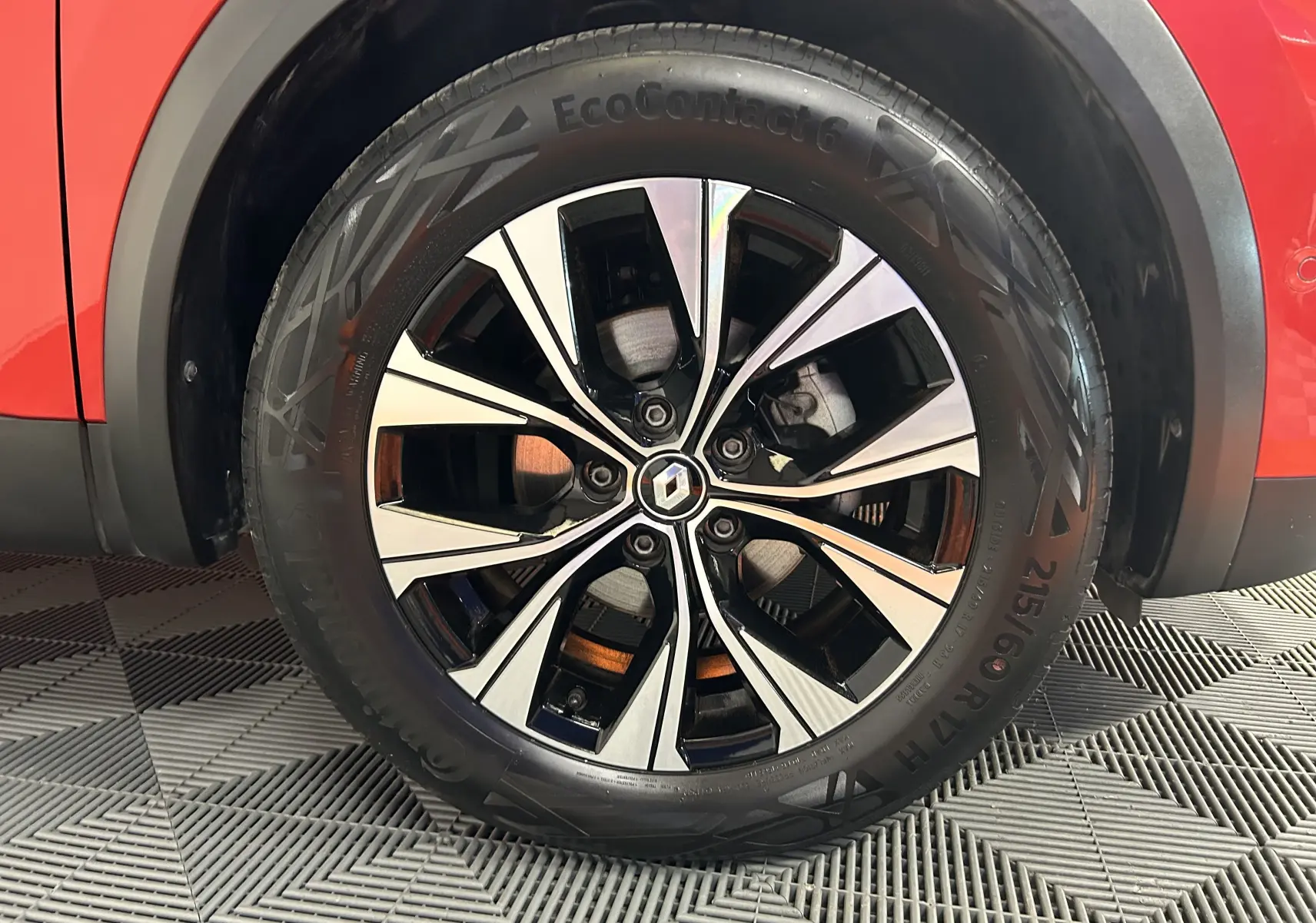 Gros plan sur la roue avant droite du Renault Captur rouge flamme métal avec jante alliage noir et argentée au design moderne.