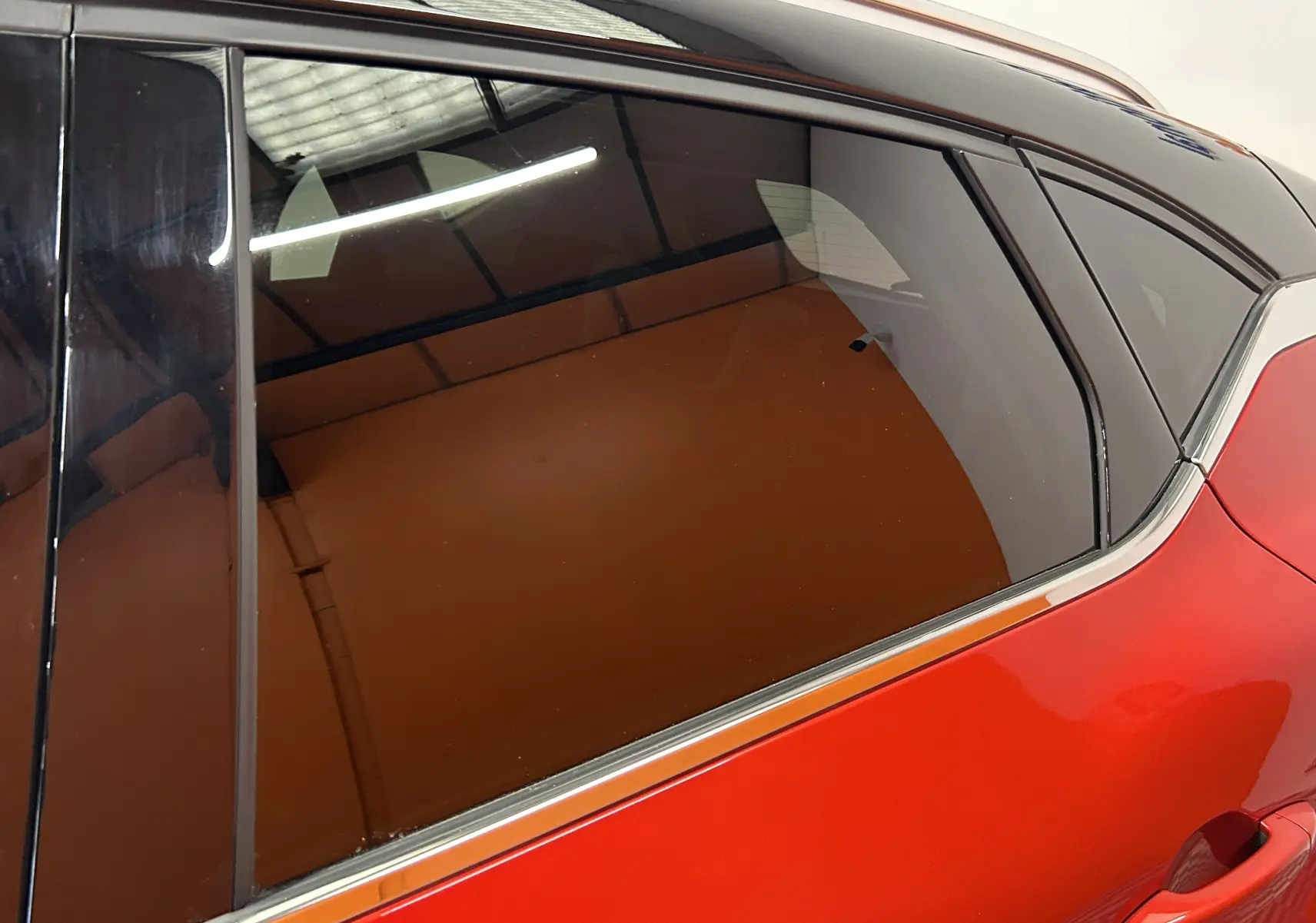 Gros plan sur la vitre arrière côté droit d'un Renault Captur 2024 rouge flamme métal avec cadre chromé élégant.