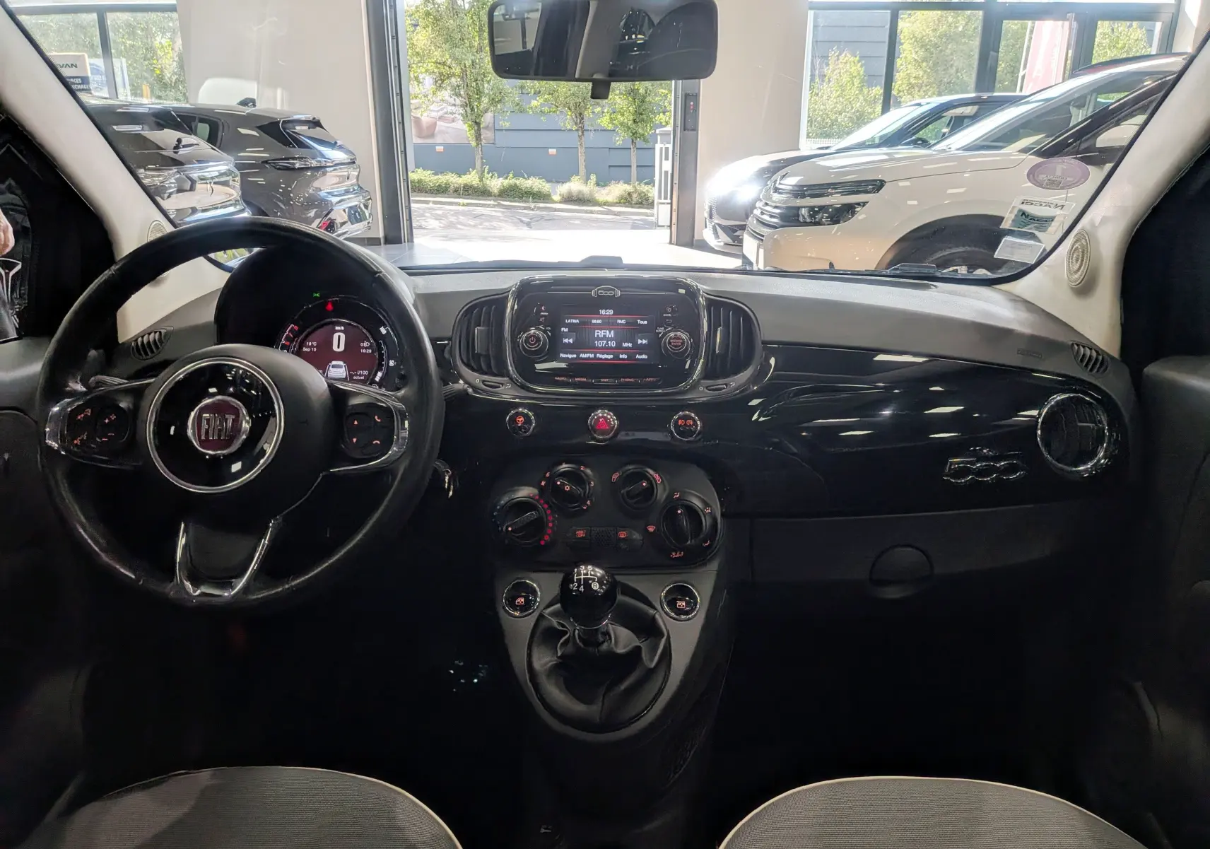 Vue intérieure frontale du tableau de bord noir brillant et volant du Fiat 500 1.2 69 CH Lounge de 2017.