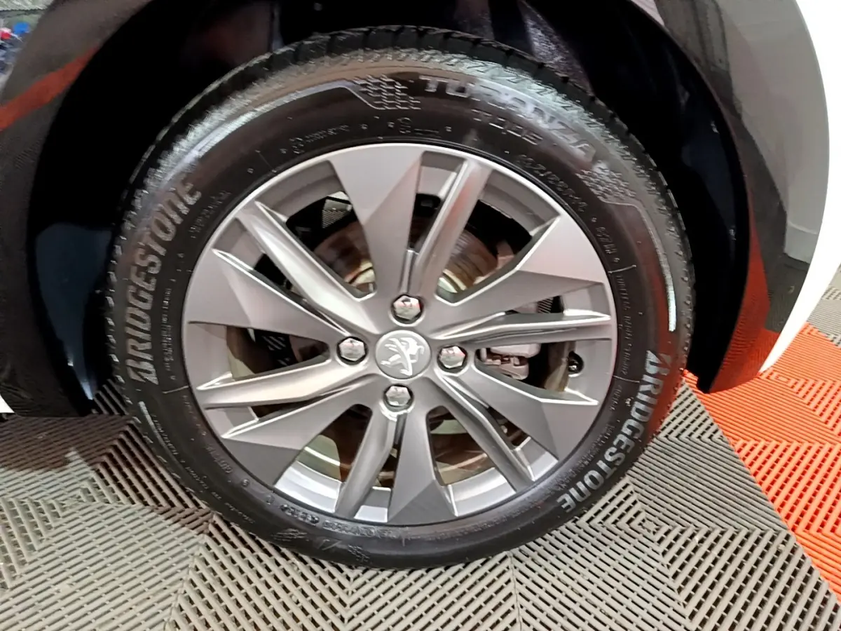 Gros plan sur la roue avant droite avec jante alliage argentée et pneu Bridgestone d'une Peugeot 208 blanche électrique.