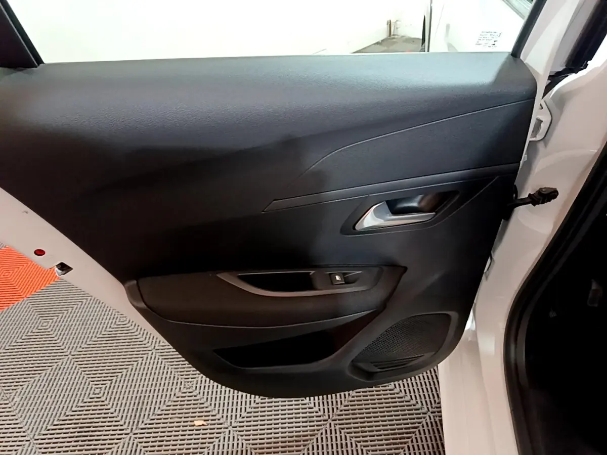 Vue rapprochée de la porte avant droite noire d'une Peugeot 208 électrique blanche, avec poignée et commande de vitre.