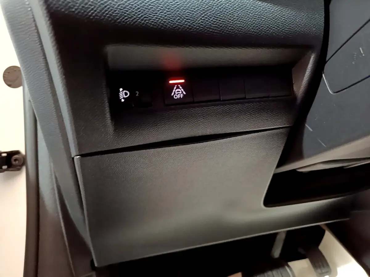 Gros plan sur les commandes noires sous le tableau de bord côté gauche d'une Peugeot 208 électrique blanche 2021.