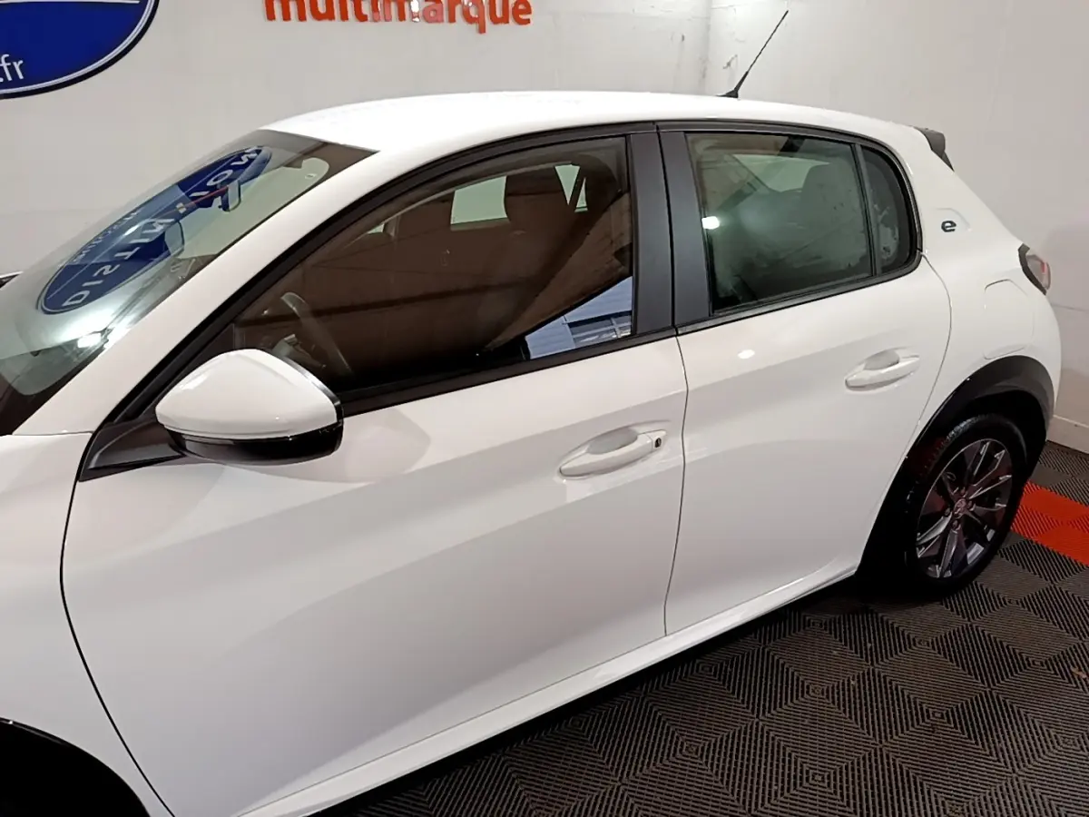 Vue latérale droite d'une Peugeot 208 électrique Active Business blanche, avec rétroviseur blanc et jantes visibles.