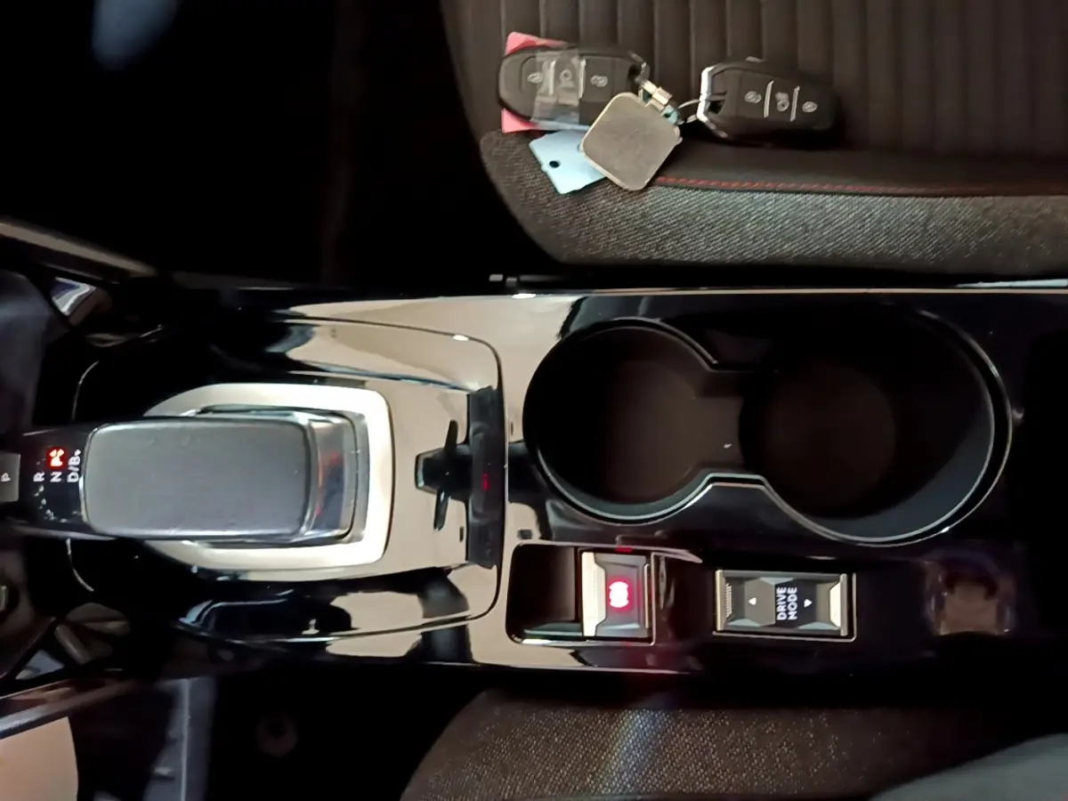 Vue plongeante sur la console centrale noire brillante avec levier de boîte auto et porte-gobelets du Peugeot 208 blanc électrique.