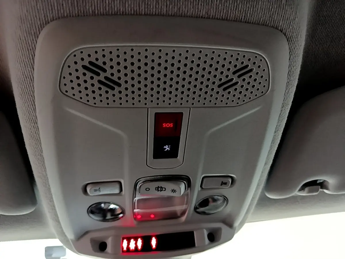 Vue en gros plan du panneau de commande au plafond intérieur gris clair du Peugeot 208 électrique, avec bouton SOS rouge éclairé.