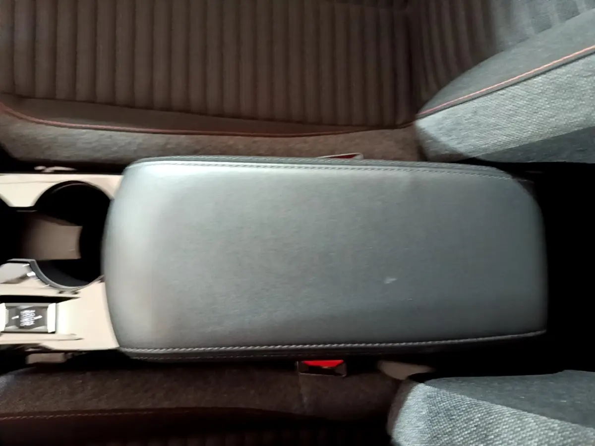 Vue plongeante sur l'accoudoir central noir et les sièges tissu gris de la Peugeot 208 électrique blanche.