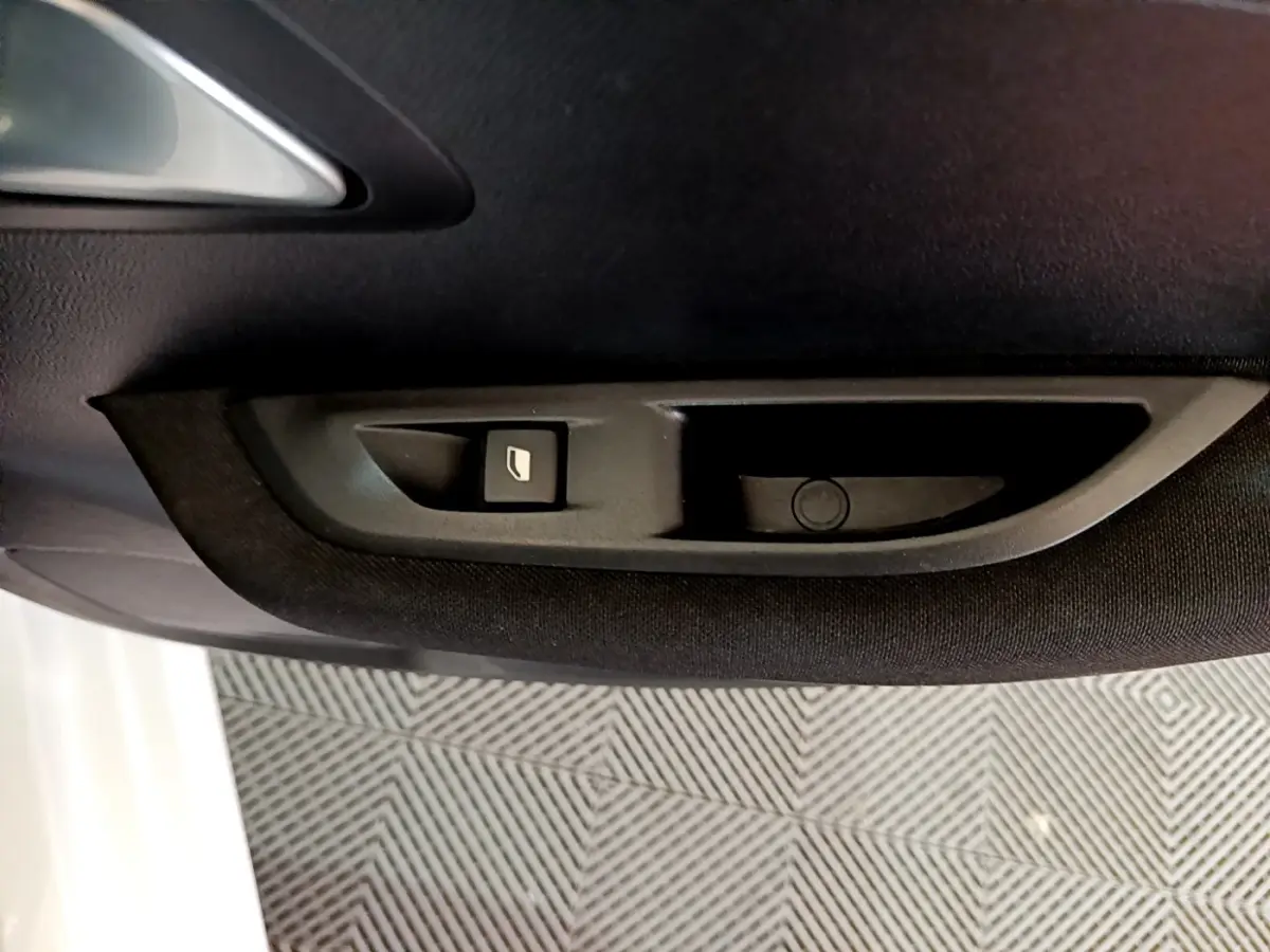 Bouton de commande de vitre sur la porte côté gauche intérieure d'une Peugeot 208 Electrique Active Business blanche.