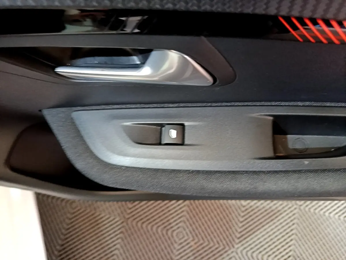 Détail de la poignée intérieure et commande de lève-vitre côté gauche d'une Peugeot 208 électrique blanche.